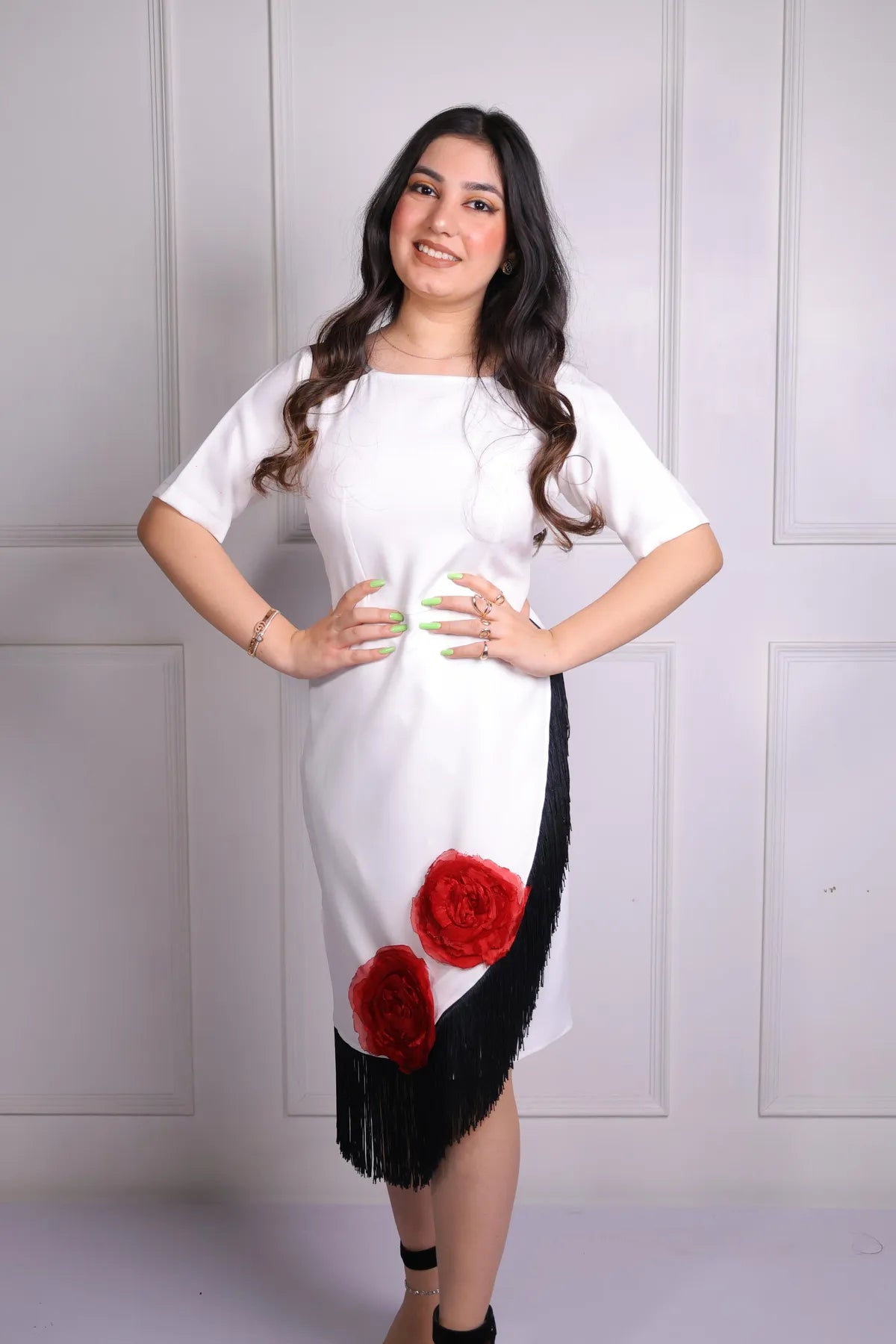 Woman wearing a white dress with red floral designs and black fringe against a white background