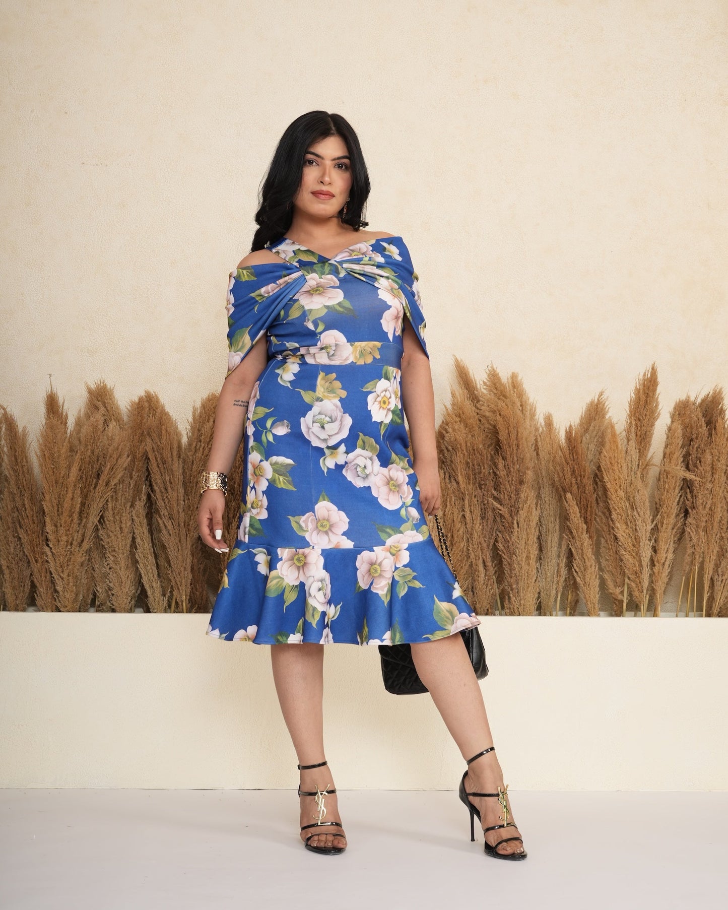 Woman wearing a blue floral dress standing in front of a beige wall with dried grass.