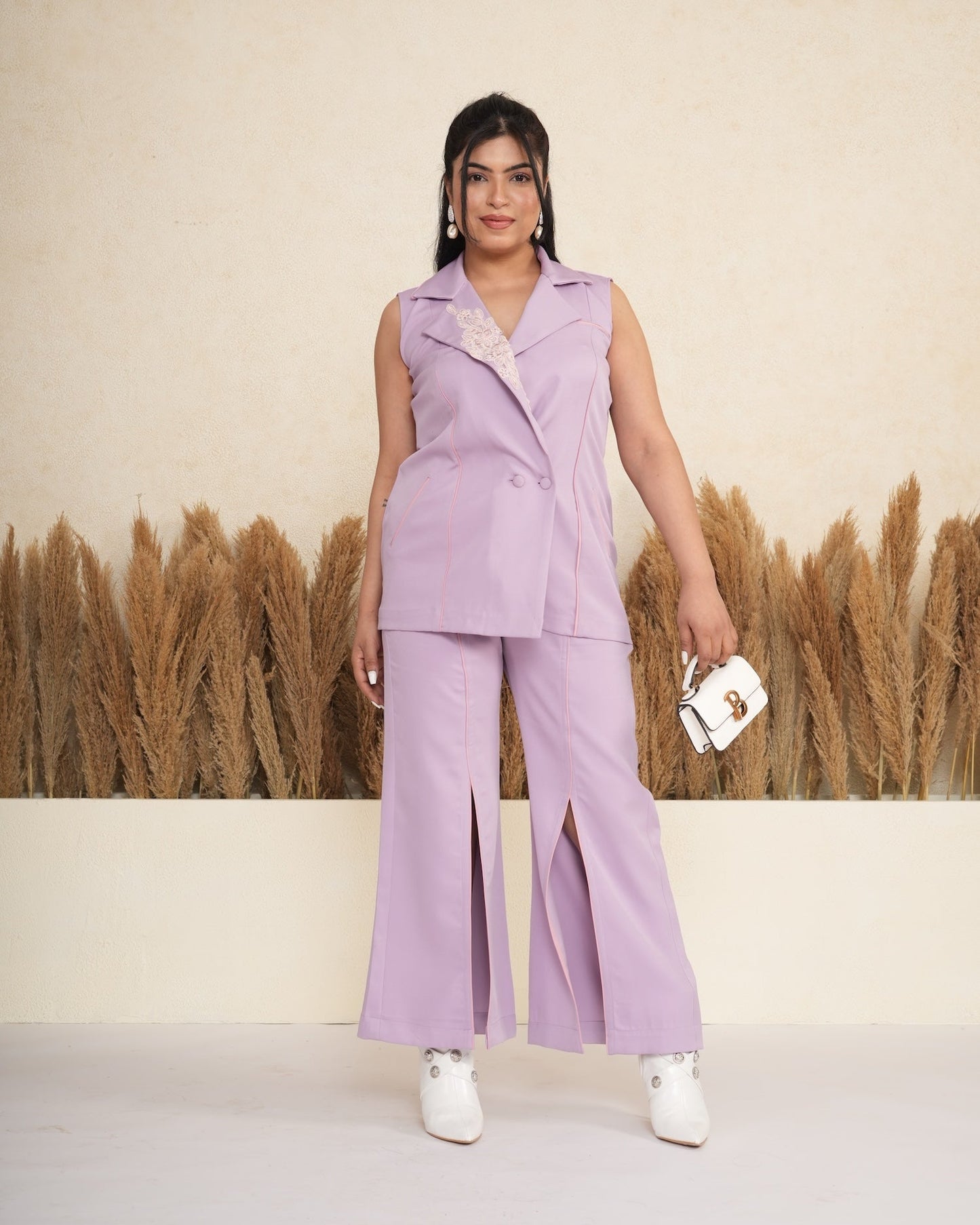 Woman in a lavender outfit standing in front of a decorative wall with plants.