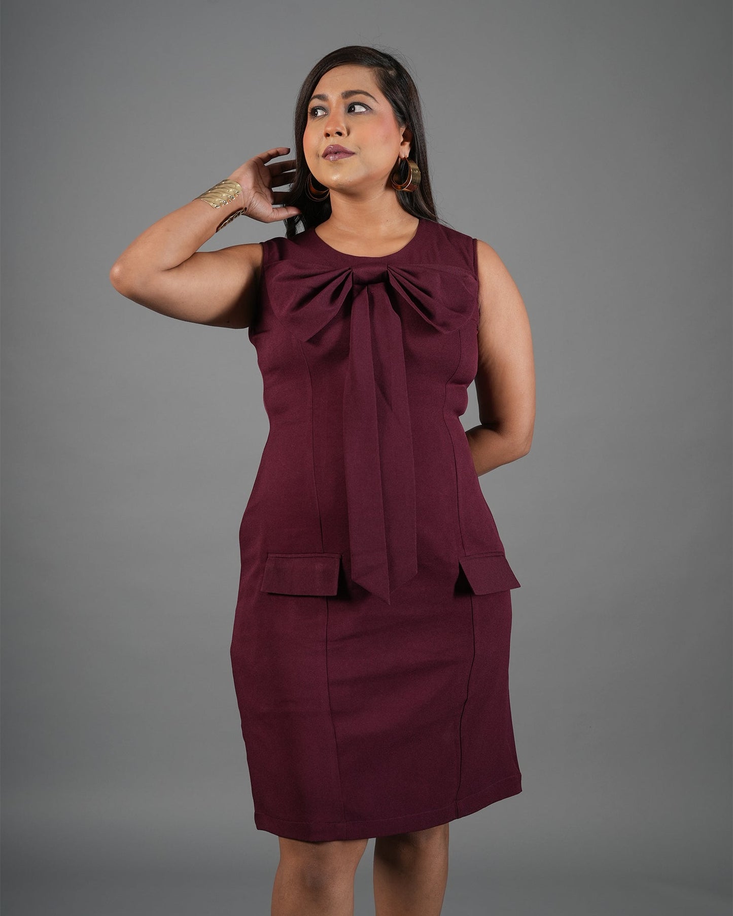 Woman wearing a burgundy dress with a bow detail on a gray background