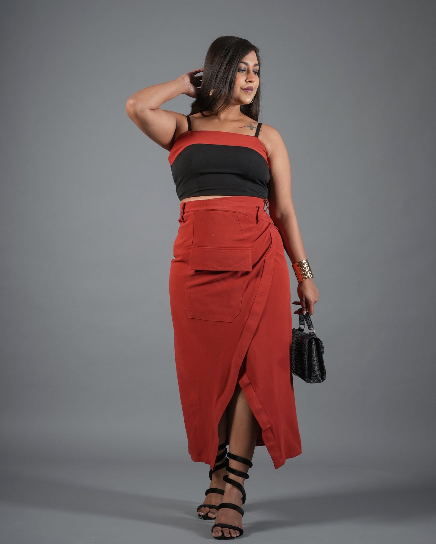 Woman wearing a black top and red skirt against a gray background