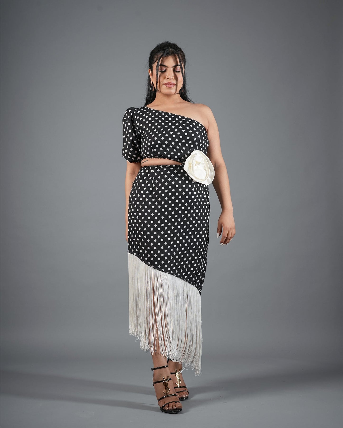 Woman wearing a black and white polka dot dress with a sheer white skirt on a gray background
