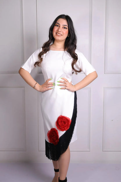 Woman wearing a white dress with red floral designs and black fringe against a white background