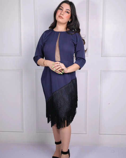 Woman wearing a navy blue top with a black fringed skirt against a white paneled wall.