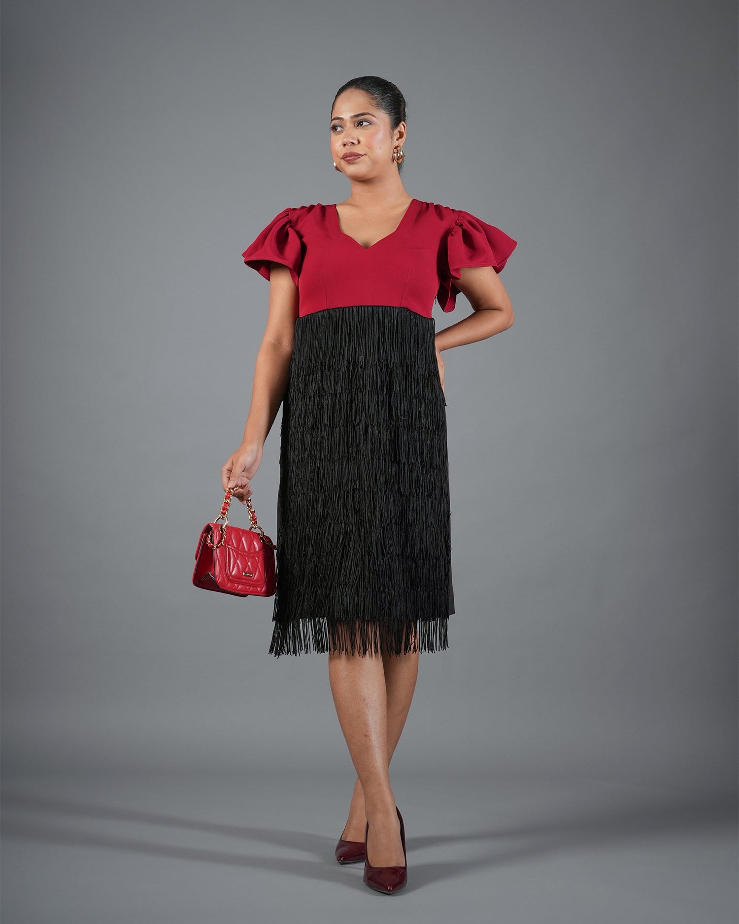 Woman wearing a red top and black fringed skirt with a red handbag on a gray background
