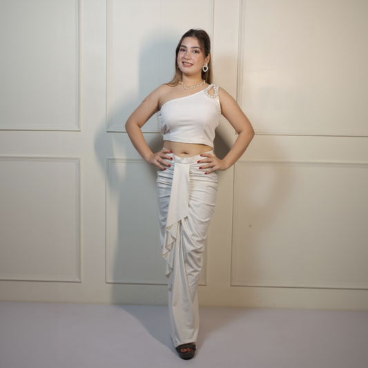 Woman wearing a white one-shoulder top and beige dhoti against a plain background