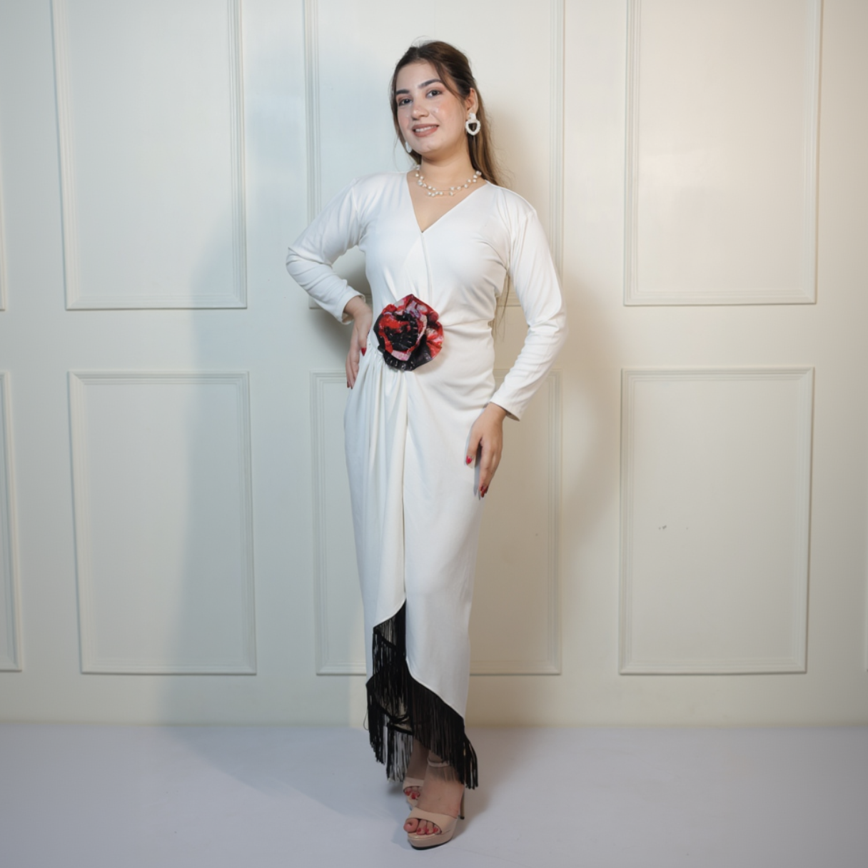 Woman wearing a white dress with black fringe and a red flower accessory against a white background